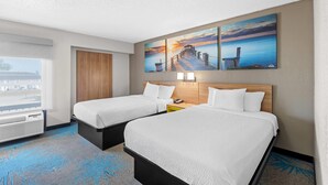 A hotel room with two beds, a wooden headboard, a large window, and a painting of a sunset over a pier. - Days Inn & Suites by Wyndham Cedar Rapids (Cedar Rapids)