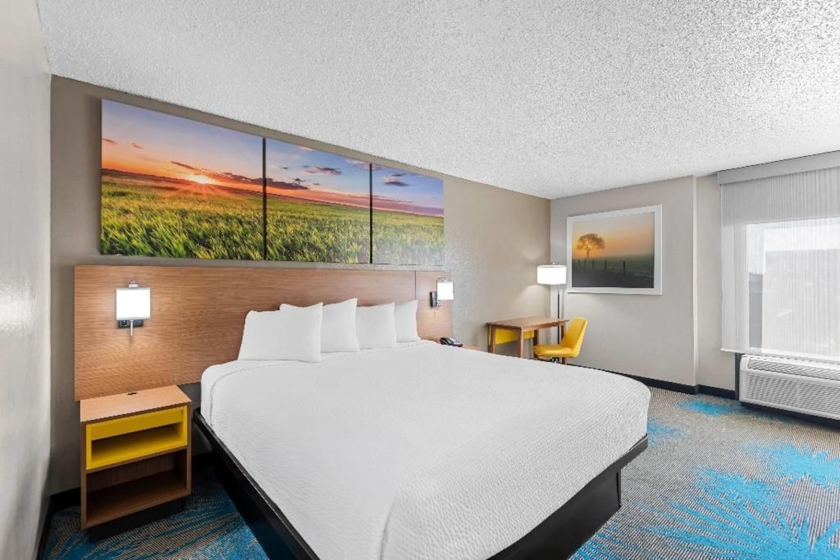 A hotel room with a large bed, a nightstand, a desk, a chair, and a window with curtains.