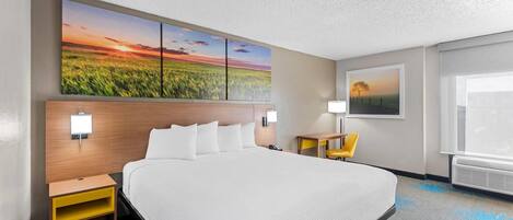 A hotel room with a large bed, a nightstand, a desk, a chair, a painting, and a window.
