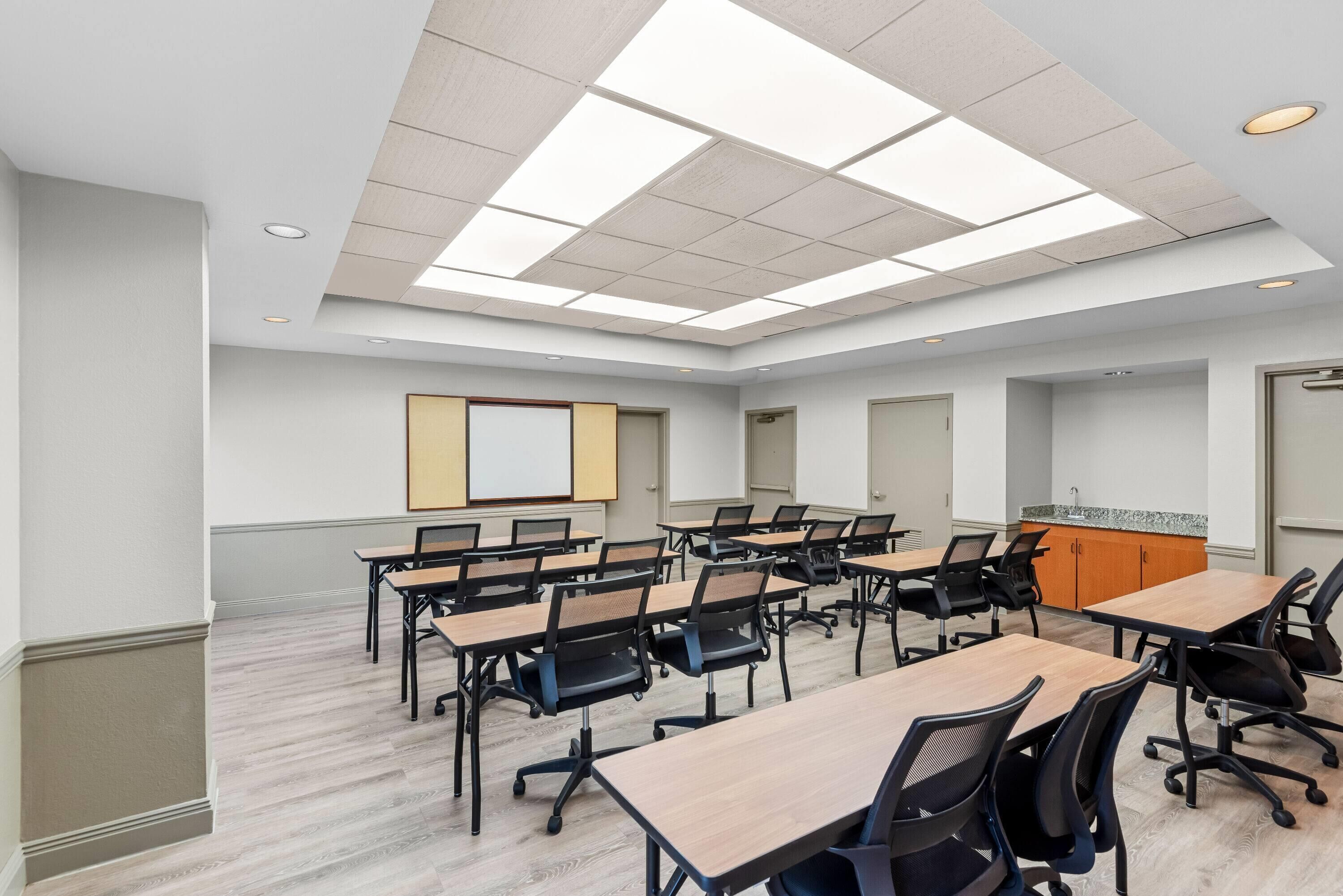 A conference room with multiple tables and chairs, a whiteboard, and a projector screen.