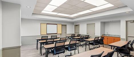 A conference room with multiple tables and chairs, a whiteboard, and a projector screen.