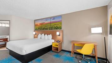 A hotel room with a bed, a desk, a chair, a nightstand, a lamp, and a wall art piece.
