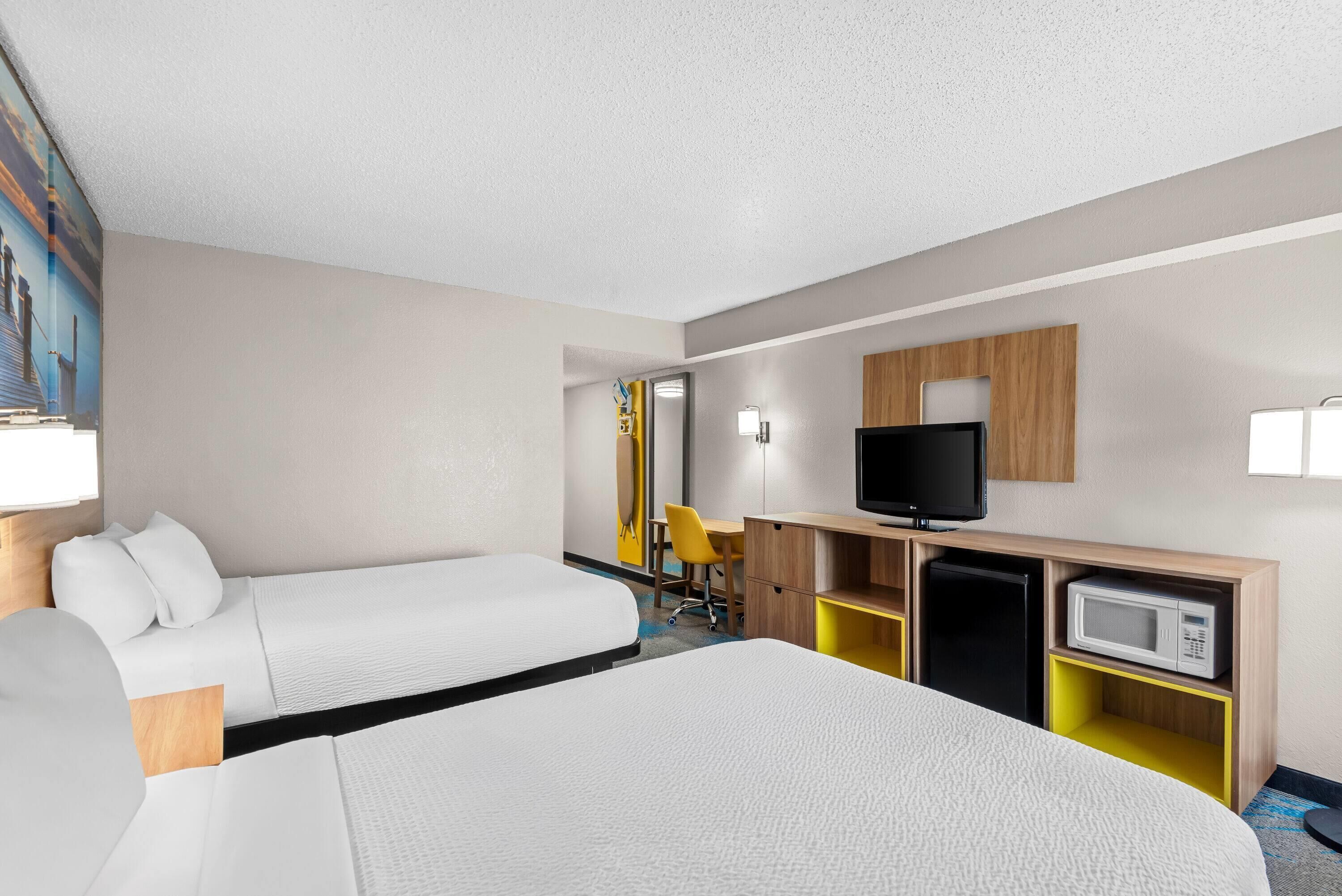 Habitación de hotel con dos camas, un escritorio, una silla, un televisor y un microondas.
