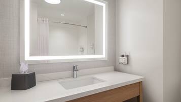 Een badkamer met een wit wastafel, een spiegel met verlichting en een douchegordijn.