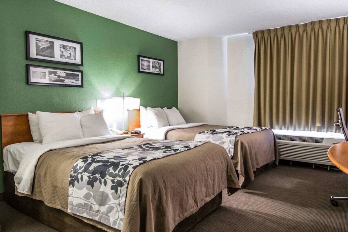 A hotel room with two beds, a green wall, and a window with curtains.