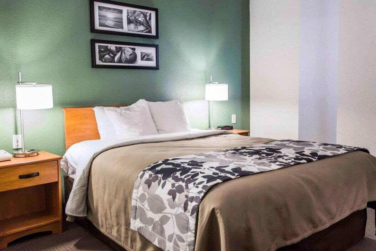 A hotel room with a bed, two bedside lamps, a nightstand, a wooden headboard, and two framed pictures on the wall.