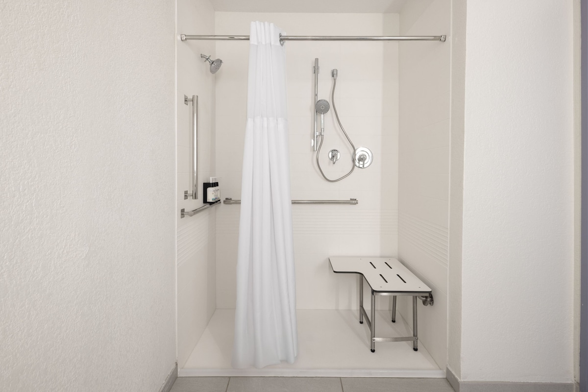 A modern shower area with a white showerhead, a handheld showerhead, a glass shower enclosure, and a bench.