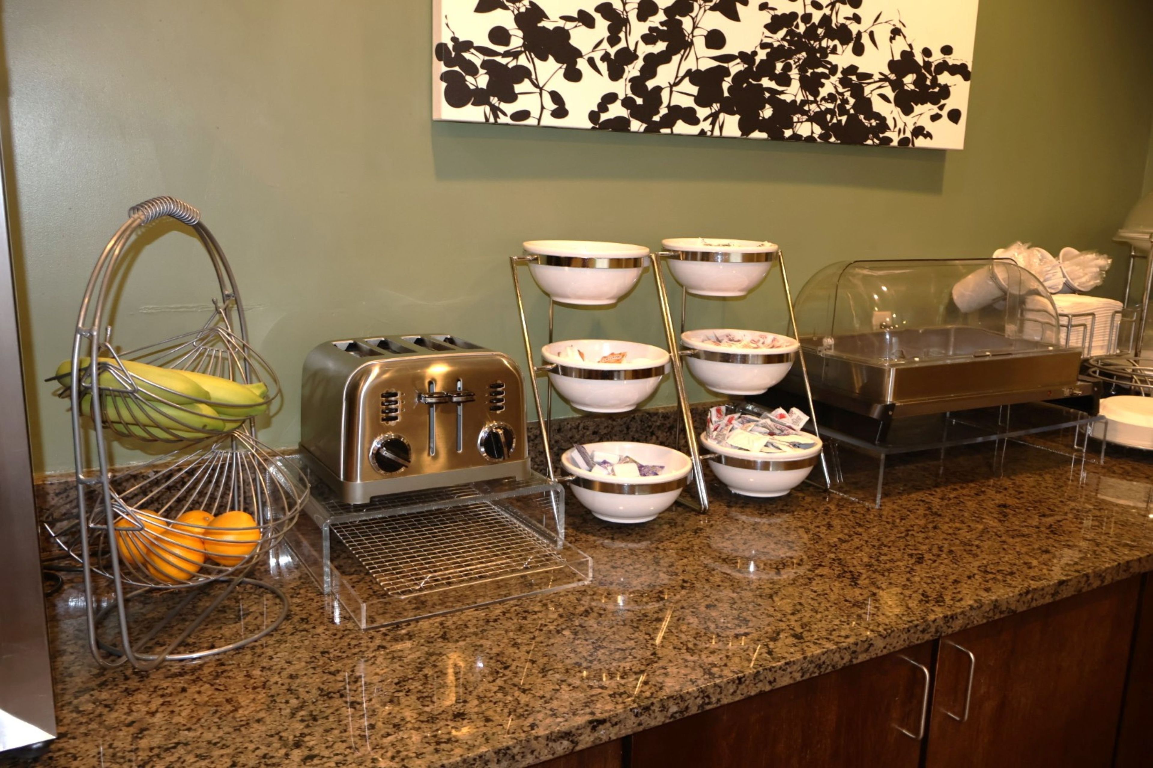 A kitchen counter with a toaster, a fruit basket, and a buffet setup with bowls and a food display case.