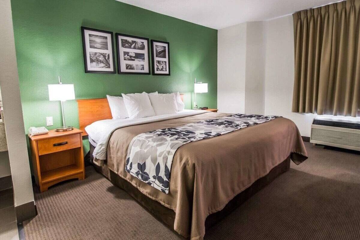 A hotel room with a bed, two bedside tables, a lamp, a wall with three framed pictures, and a window with curtains.