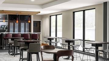 A modern restaurant with a bar area, multiple seating options including tables and chairs, and large windows providing natural light.