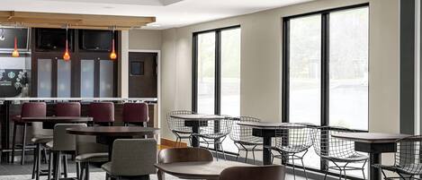 A modern restaurant with a bar area, multiple seating options including tables and chairs, and large windows providing natural light.