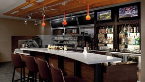 A modern kitchen with a bar area, equipped with bar stools, a large island, and a television displaying a sports event.