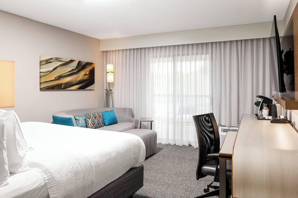 A hotel room with two beds, a desk, a chair, a lamp, and a painting on the wall.