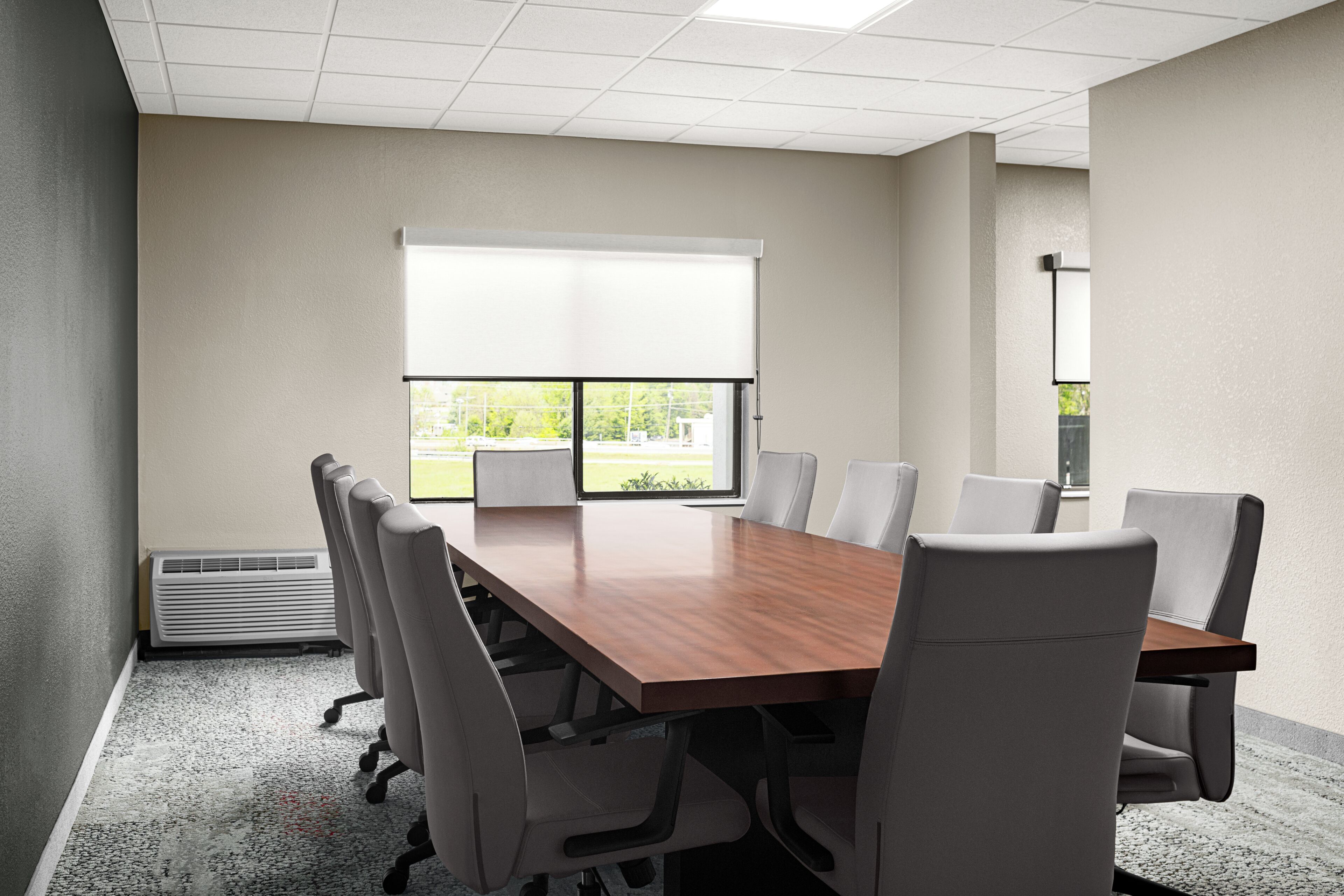 A conference room with a wooden table, six chairs, a large window, and a ceiling light fixture.
