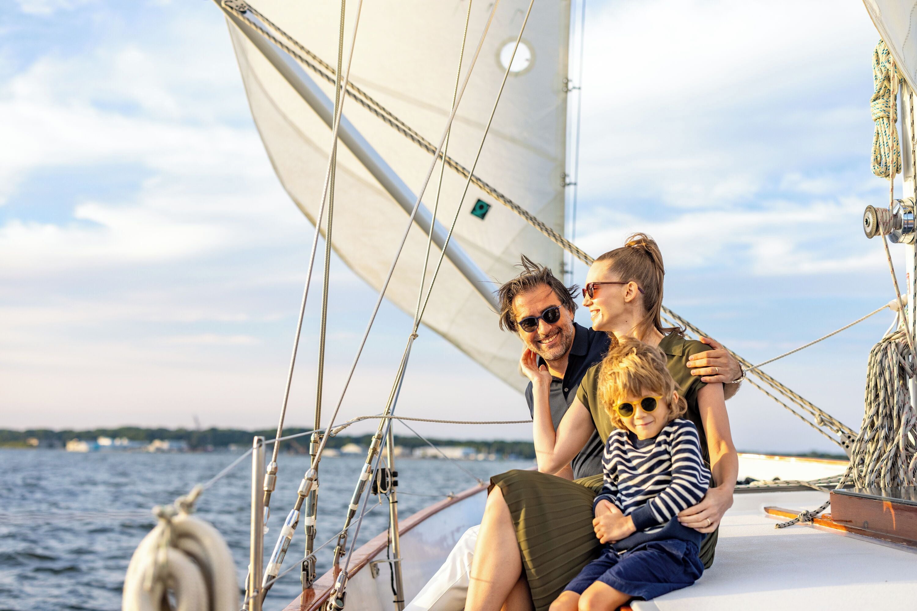 A family on a sailboat with a view of the water and distant land.