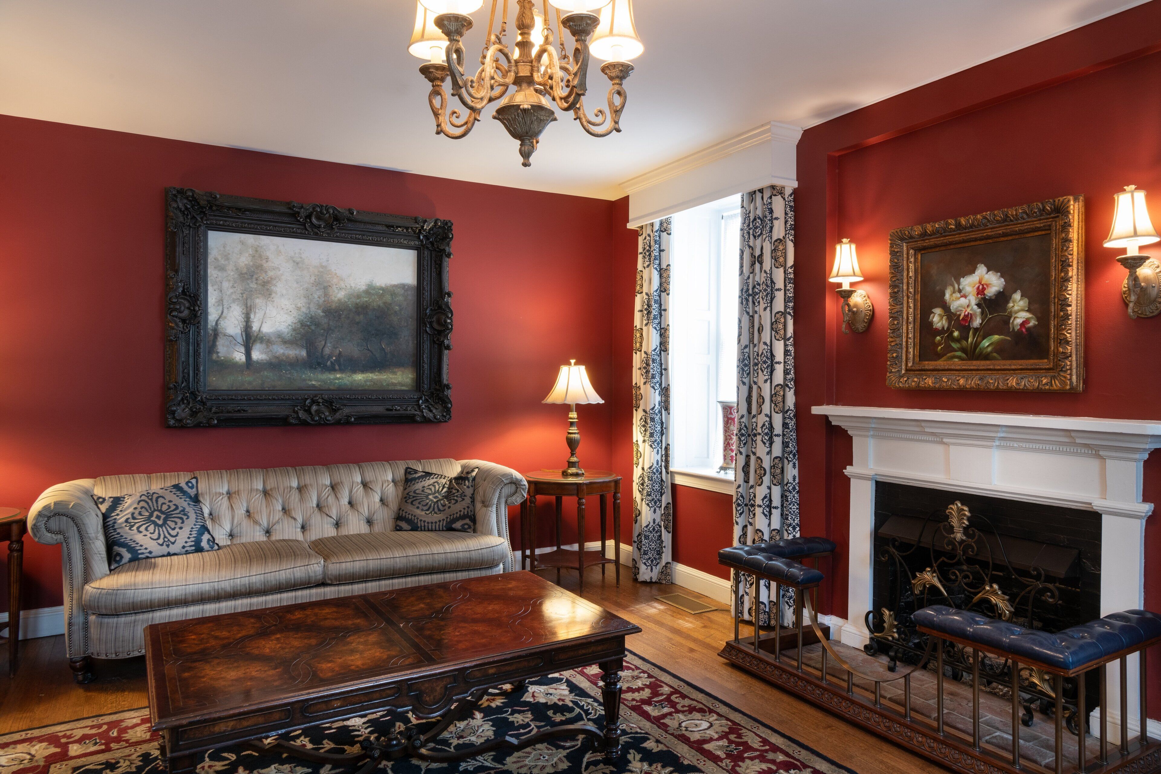 A traditional living room with a red wall, a large painting, a fireplace, and a chandelier.