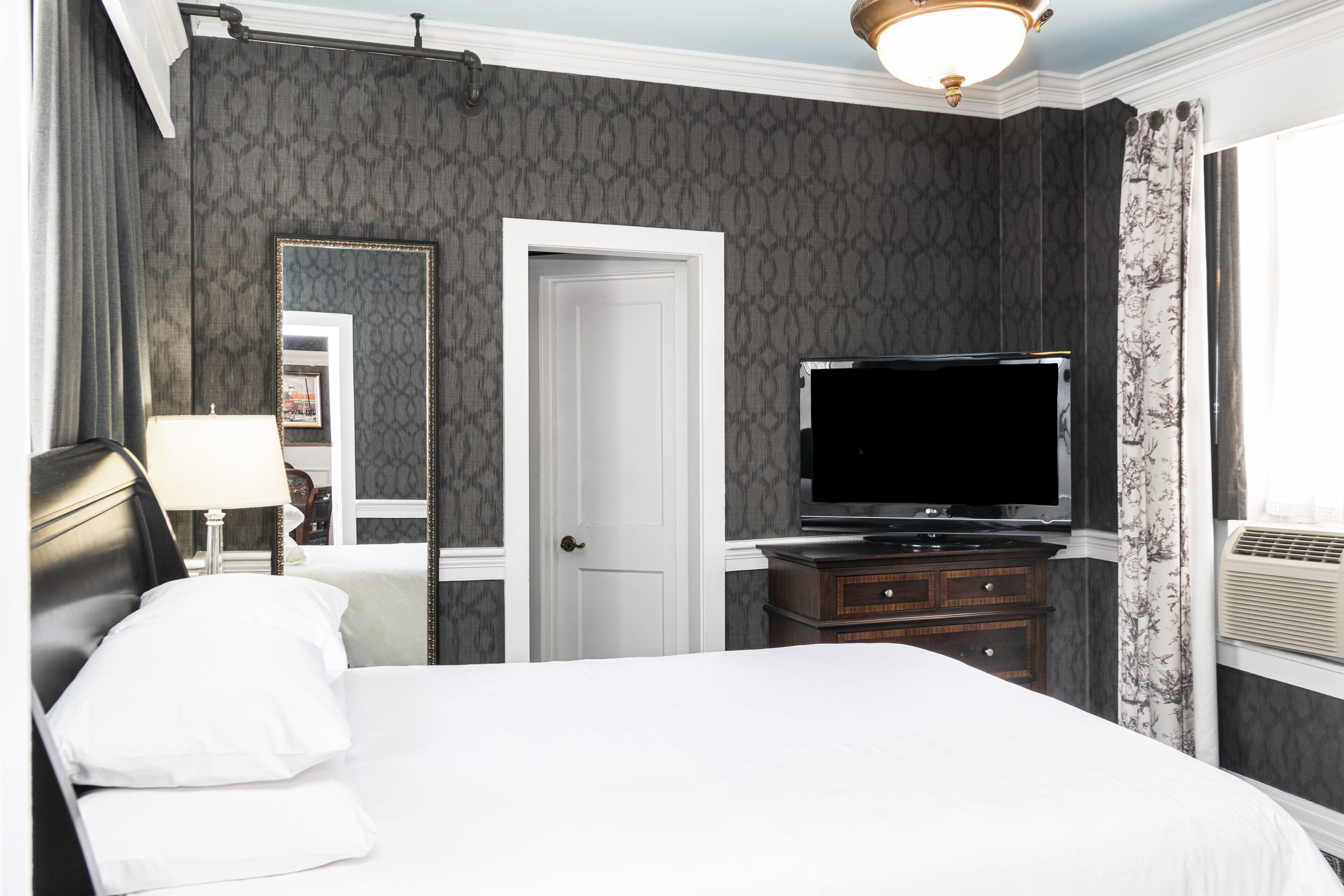 Una habitación de hotel con una cama, televisión, cómoda y espejo.