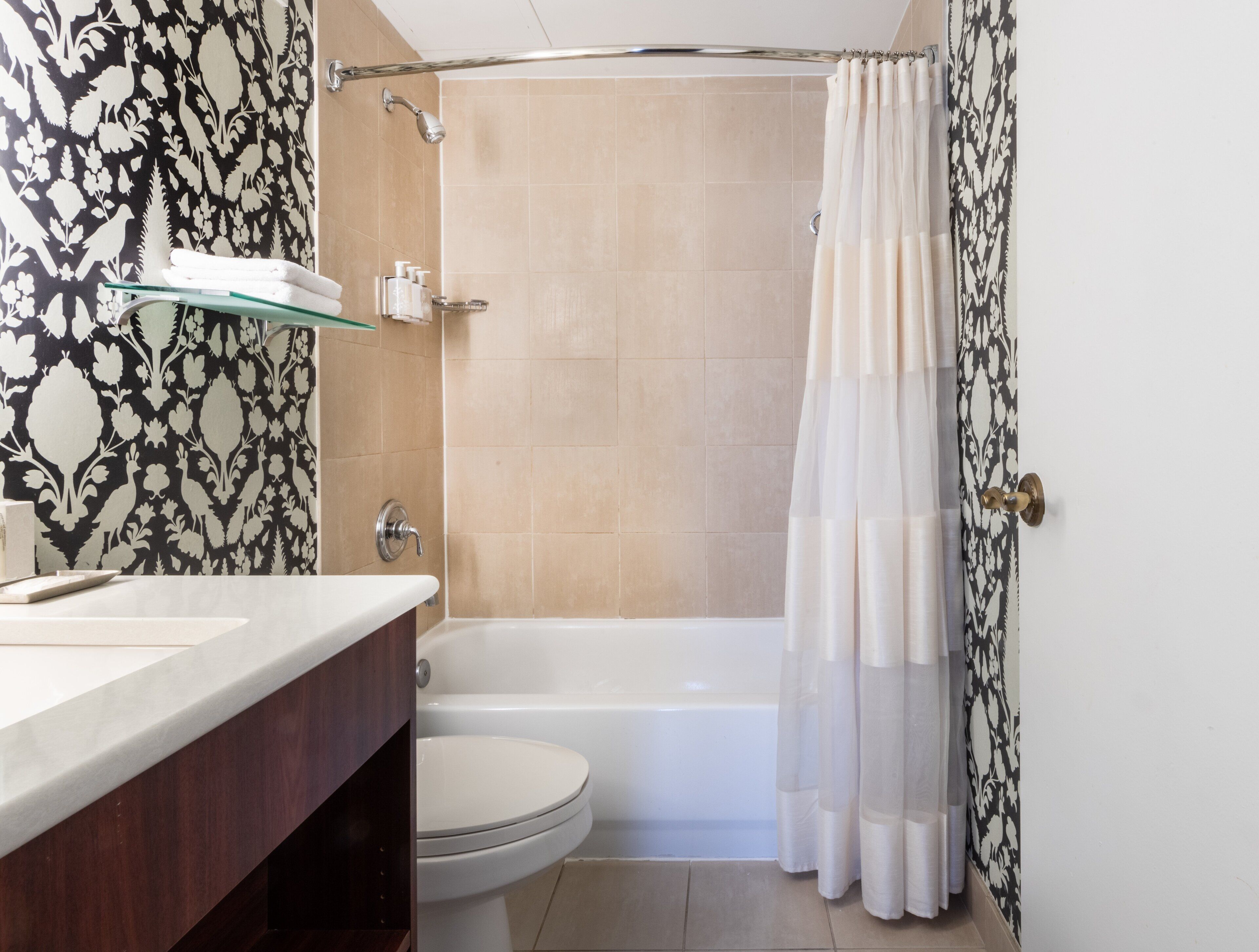 Une salle de bain équipée d’une baignoire, de toilettes et d’une étagère en verre où sont rangés les articles de toilette.