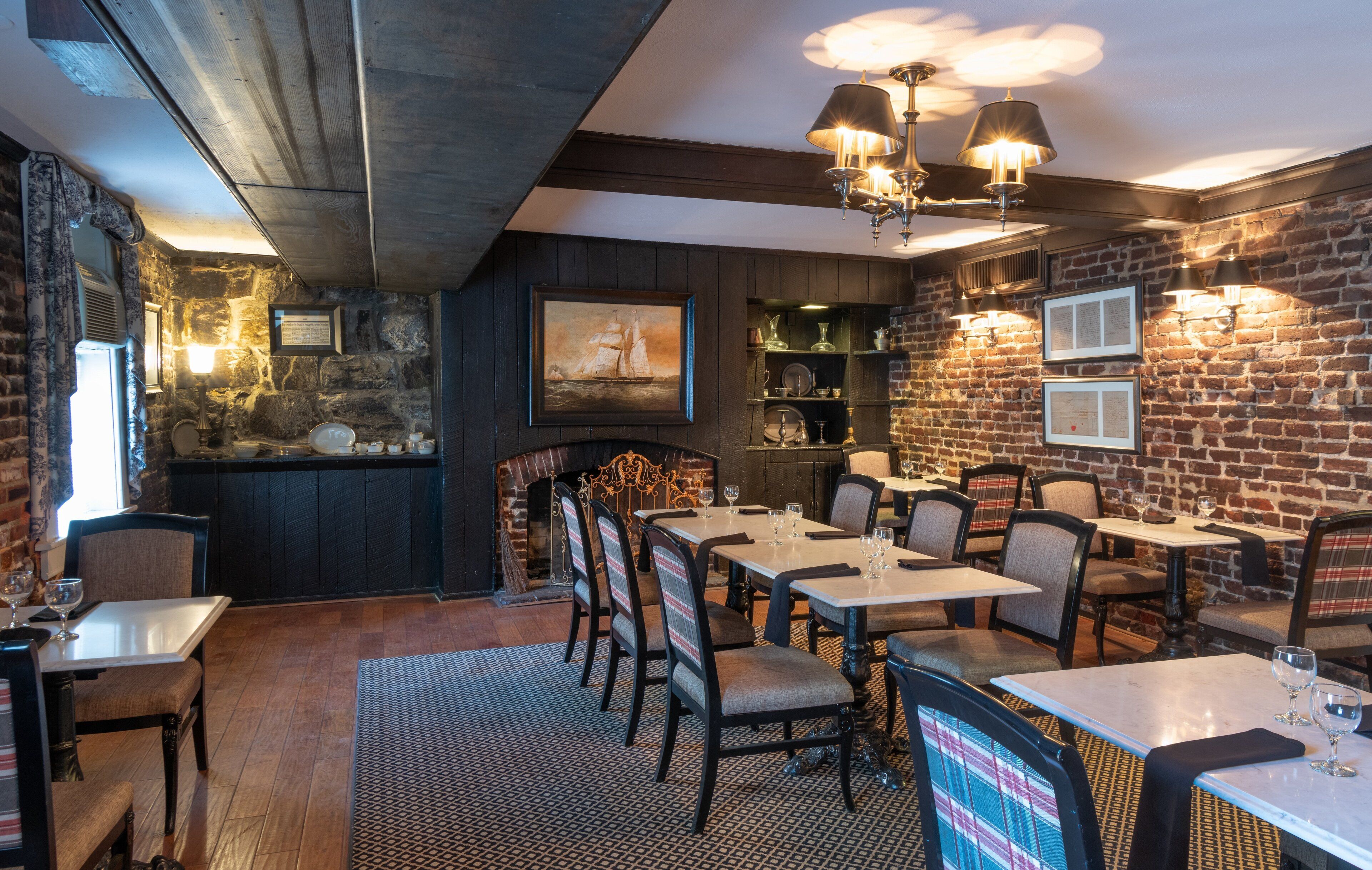 Ein Restaurant mit Backsteinwänden, Holzbalkendecke und Tischen mit Stühlen.