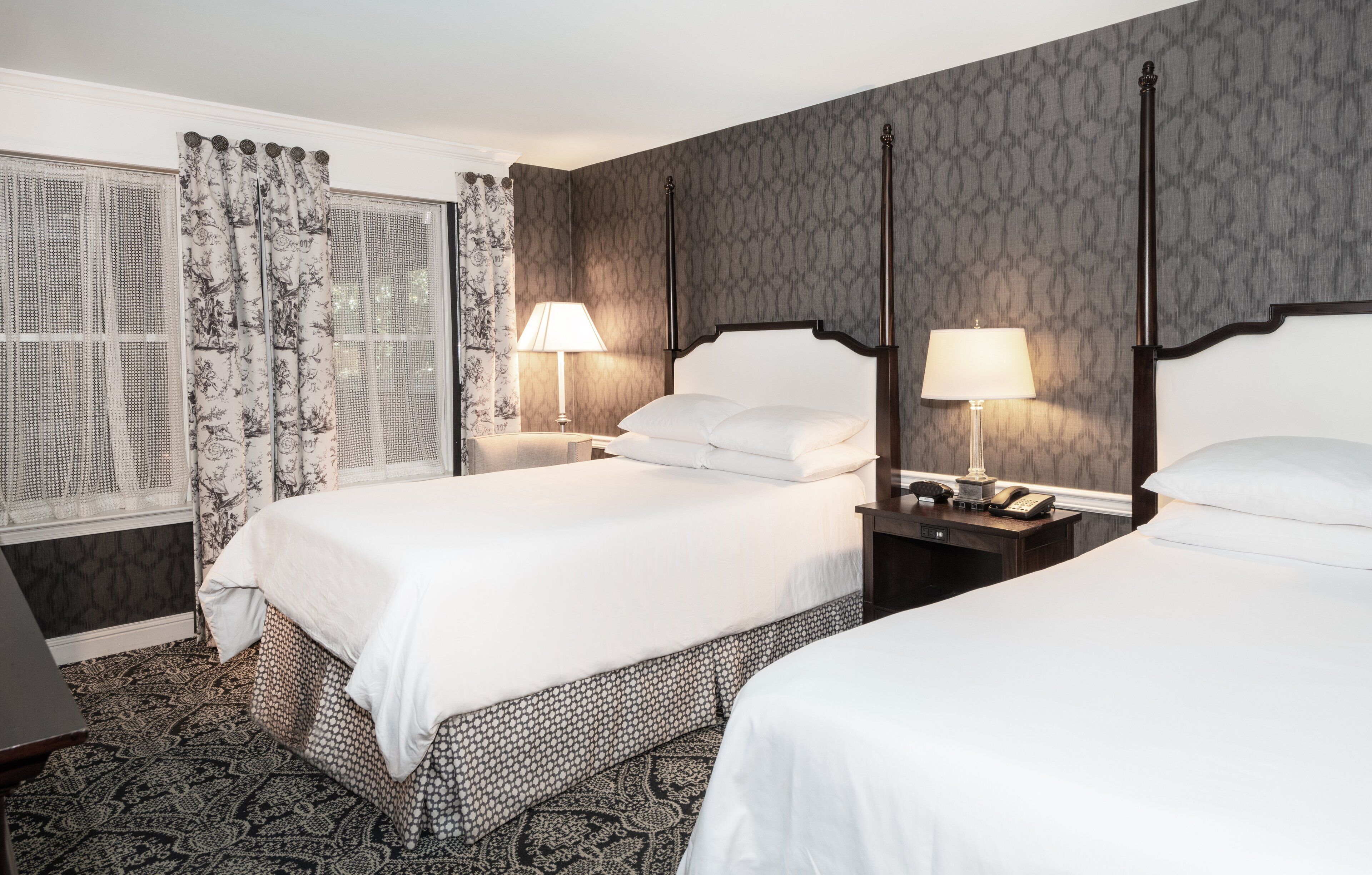 A hotel room with two beds, a window with patterned curtains, and a patterned carpet.