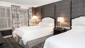 A hotel room with two beds, a window with patterned curtains, and a patterned carpet.