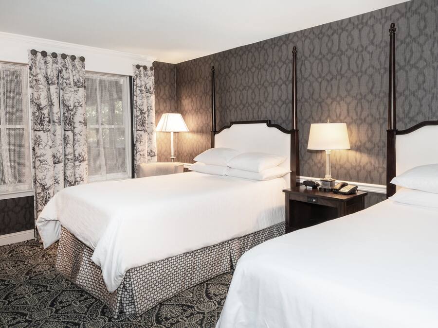 A hotel room with two beds, a window with patterned curtains, and a patterned carpet.
