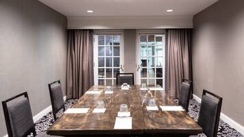 A conference room with a long table, chairs, and a view through a glass door.