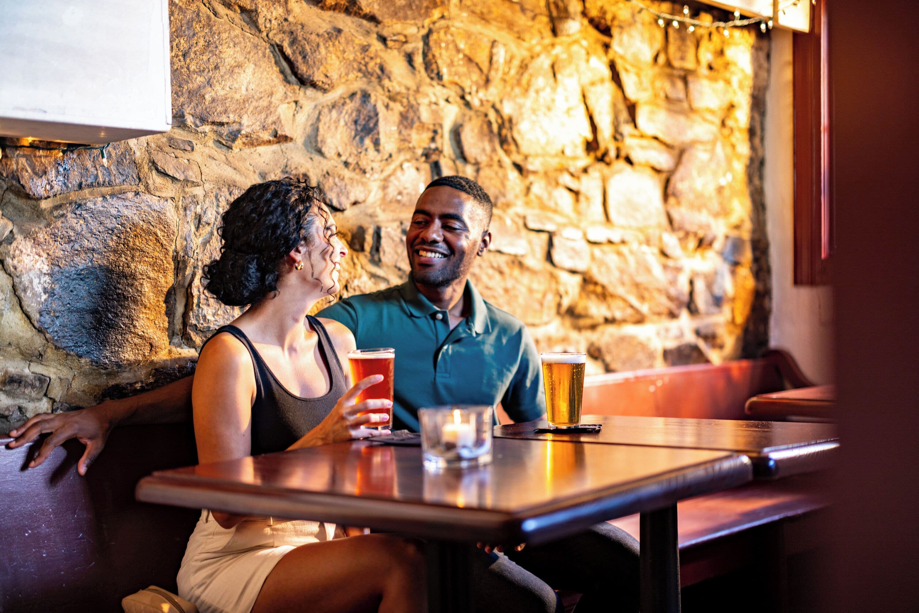 Twee personen zitten aan een tafel in een restaurant met een achtergrond van een stenen muur.