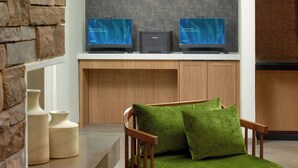 Ett modernt vardagsrum med två platt-TV-apparater på en vägg, ett träskåp under och en grön, vadderad fåtölj.