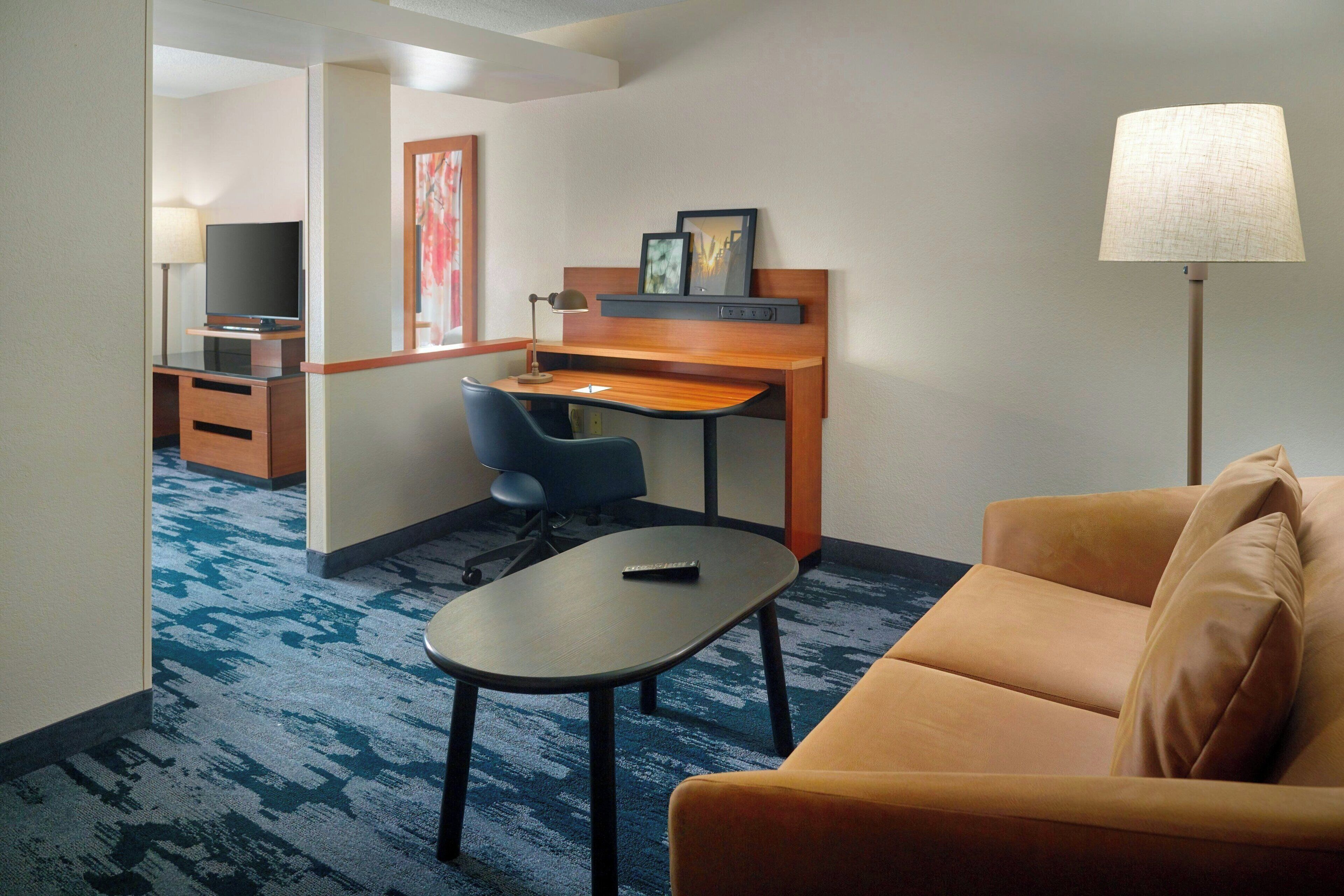 Habitación de hotel con escritorio, una silla, un sofá, un televisor y una lámpara.