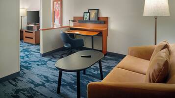 A hotel room with a desk, a chair, a sofa, a TV, and a lamp.