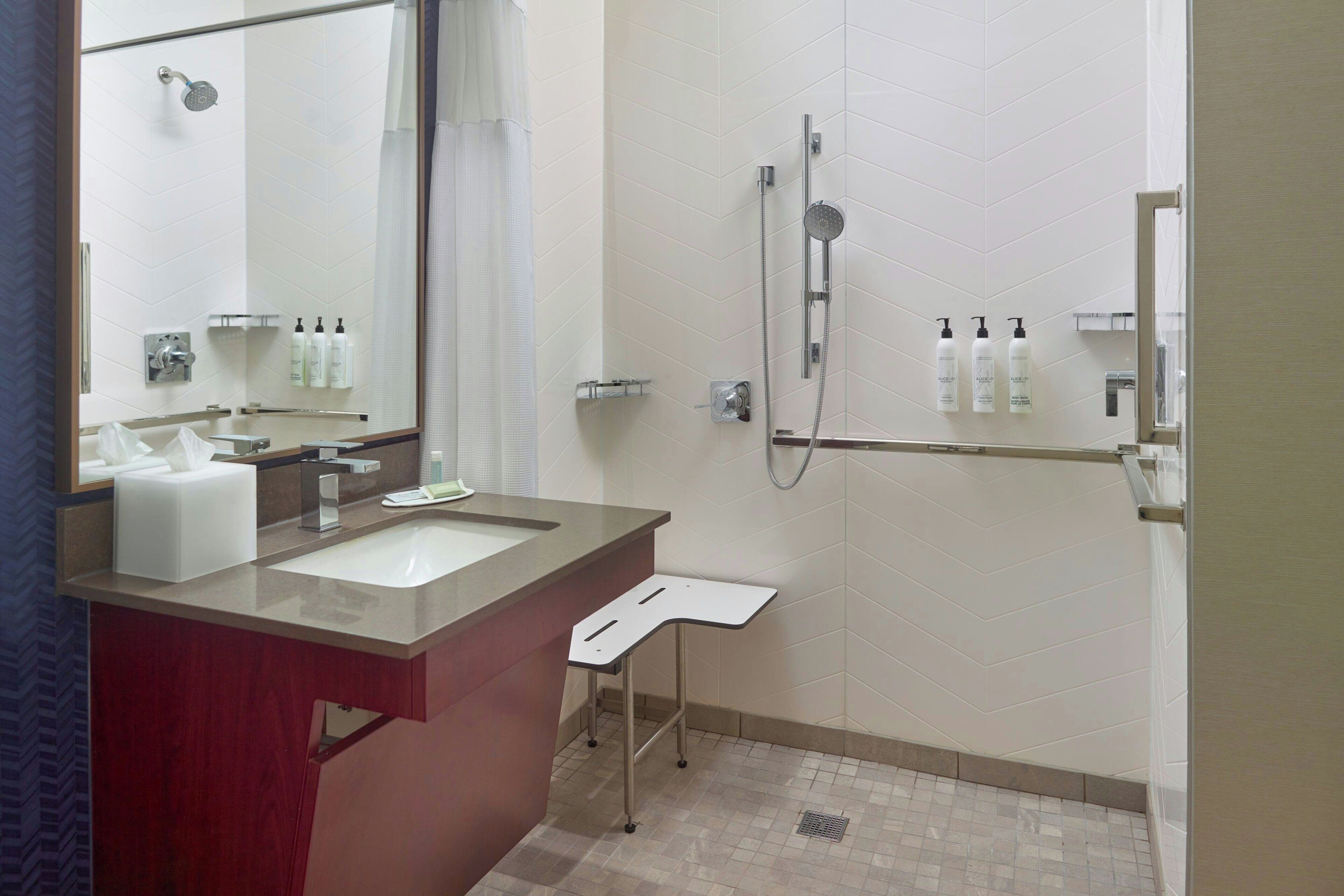 A modern bathroom with a large mirror, two sinks, a shower, and a small shelf with toiletries.