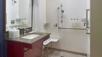 A modern bathroom with a large mirror, two sinks, a shower, and a small shelf with toiletries.