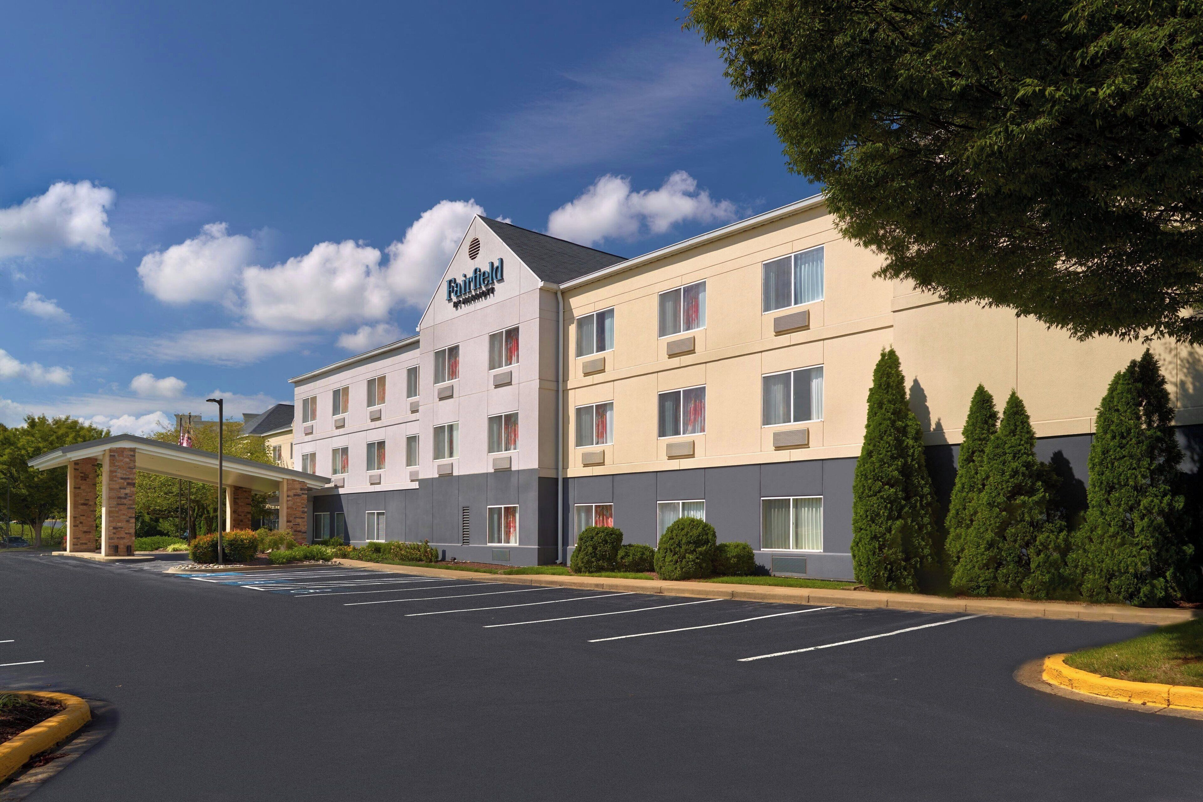 A Fairfield hotel with a modern design, featuring a covered entrance, a parking lot, and neatly arranged trees.