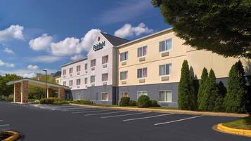A Fairfield hotel with a modern design, featuring a covered entrance, a parking lot, and neatly arranged trees.