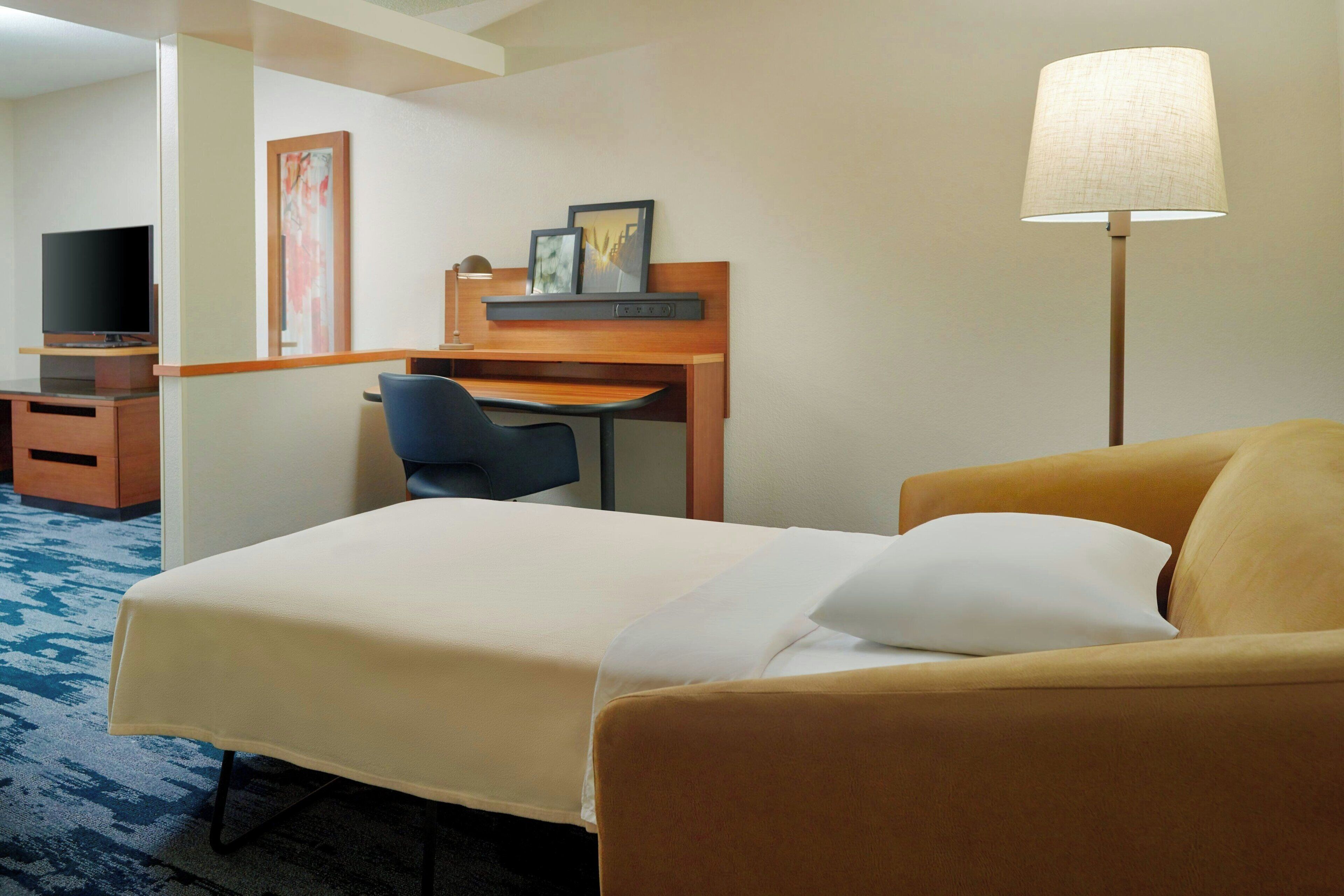 A hotel room with a bed, a desk, a chair, a television, and a lamp.