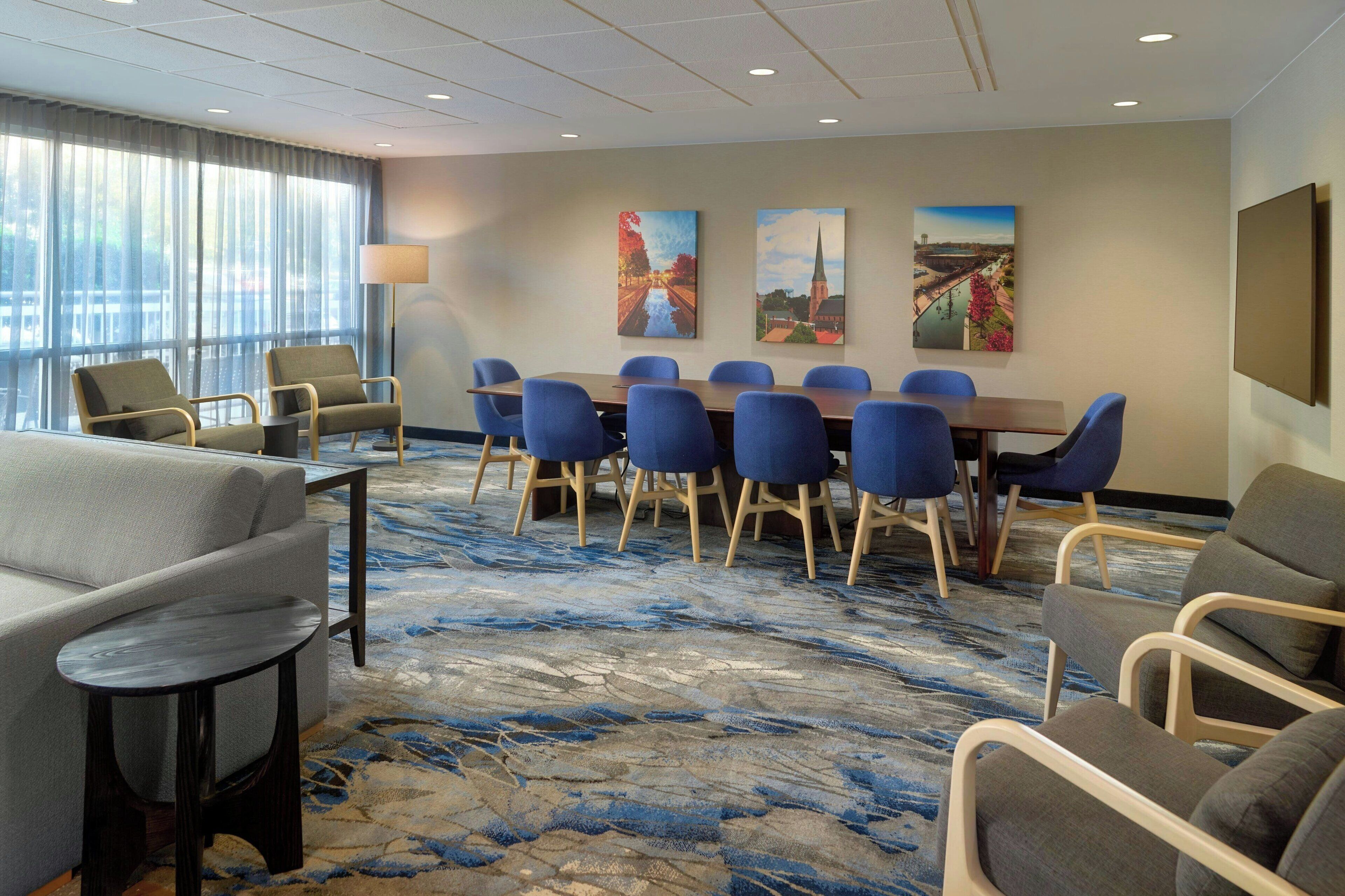 A hotel room with a large conference table, blue chairs, a sofa, and a patterned carpet.