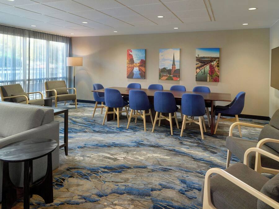 A hotel room with a large conference table, blue chairs, a sofa, and a patterned carpet.