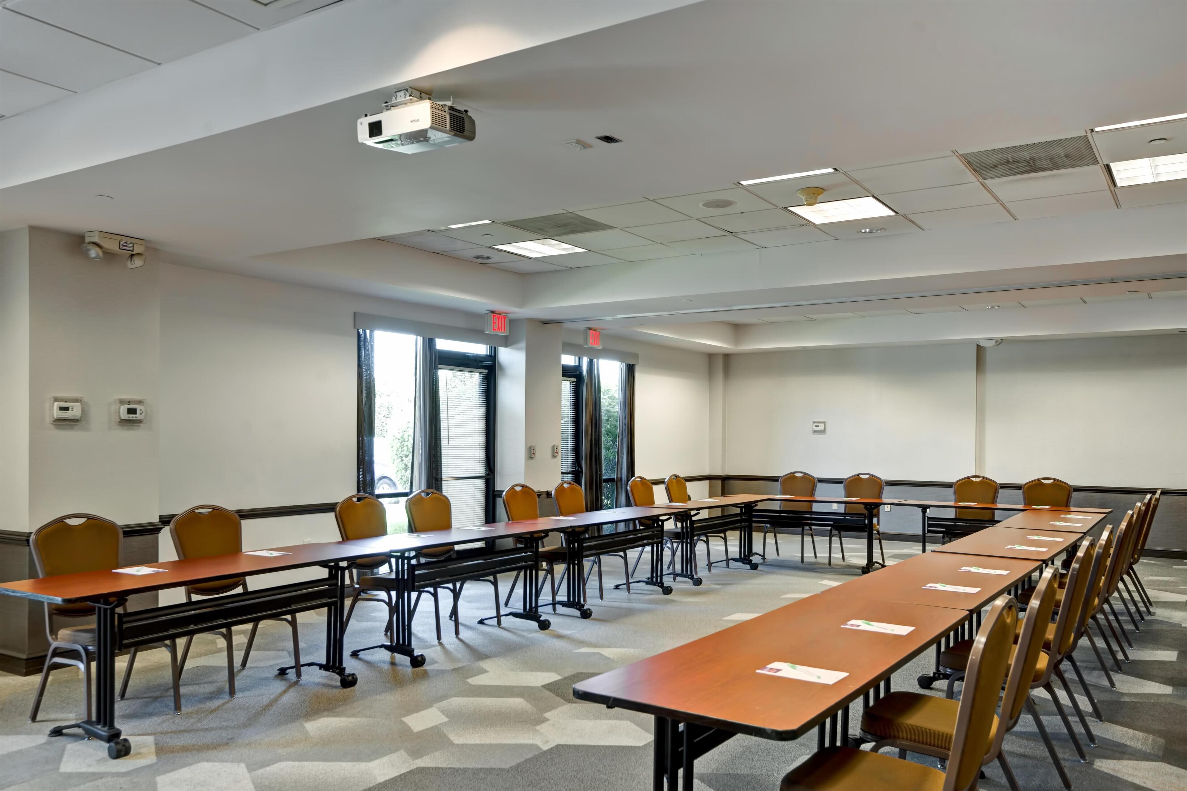 A conference room with a long table, chairs, a projector, and windows.