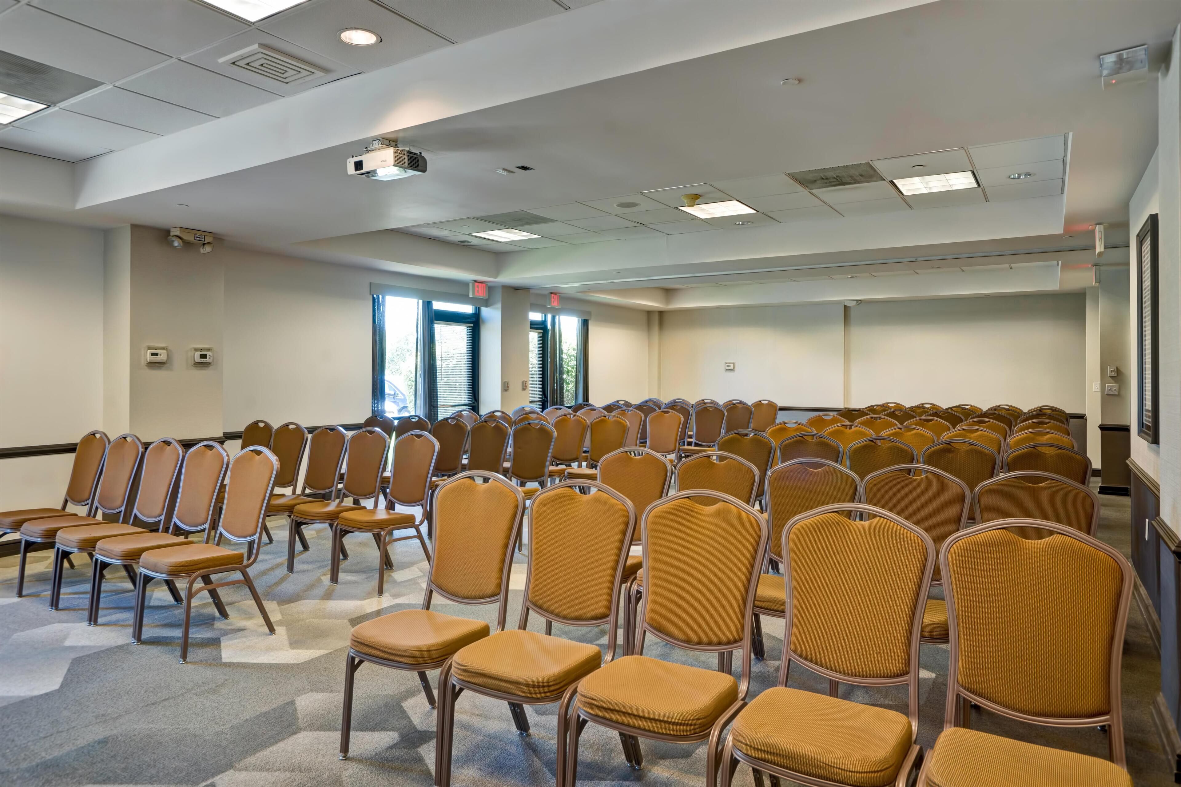 Una sala conferenze con file di sedie, luci a soffitto e finestre.