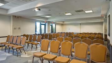 A conference room with rows of chairs, ceiling lights, and windows.