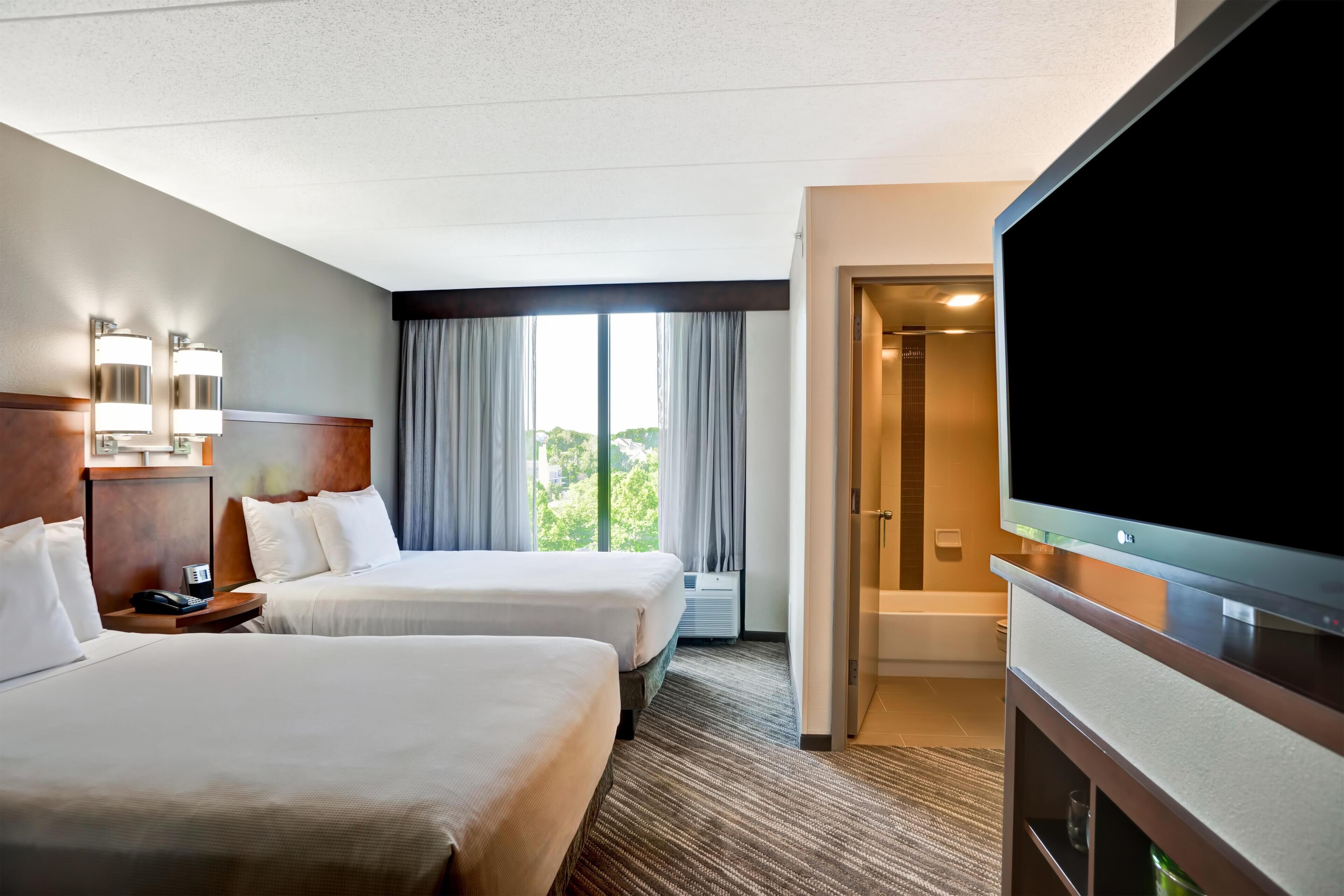 Een hotelkamer met twee bedden, een televisie, een bureau met telefoon en een raam met gordijnen.