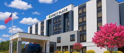 Un hotel moderno con fachada blanca, entrada cubierta y una bandera.