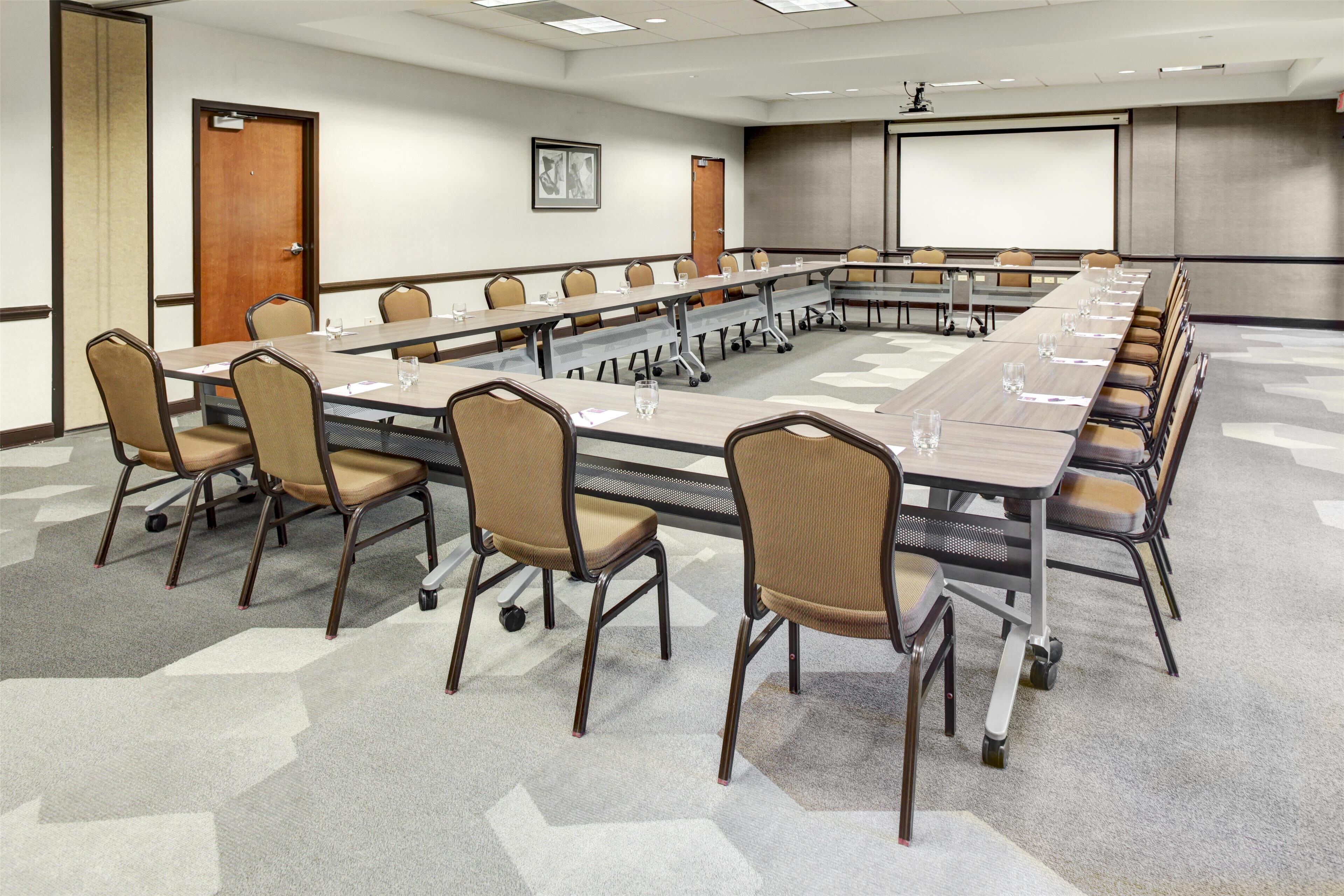 A conference room with a long table, chairs, a projector screen, and a carpeted floor.