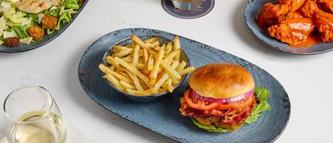 Un plato con hamburguesa, papas fritas, ensalada y alitas.