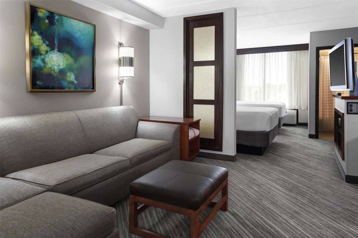 A hotel room with a sofa, a small table, a bed, a television, and a painting on the wall.