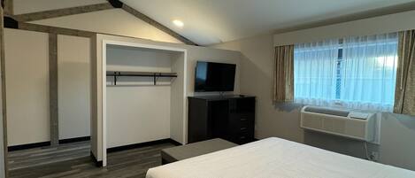 Habitación de hotel con cama, televisor, armario y ventana con cortinas.