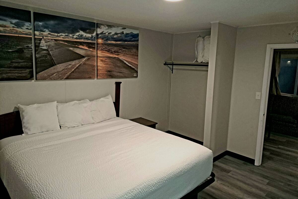 A bedroom with a bed, a nightstand, a wall-mounted shelf, and a door.