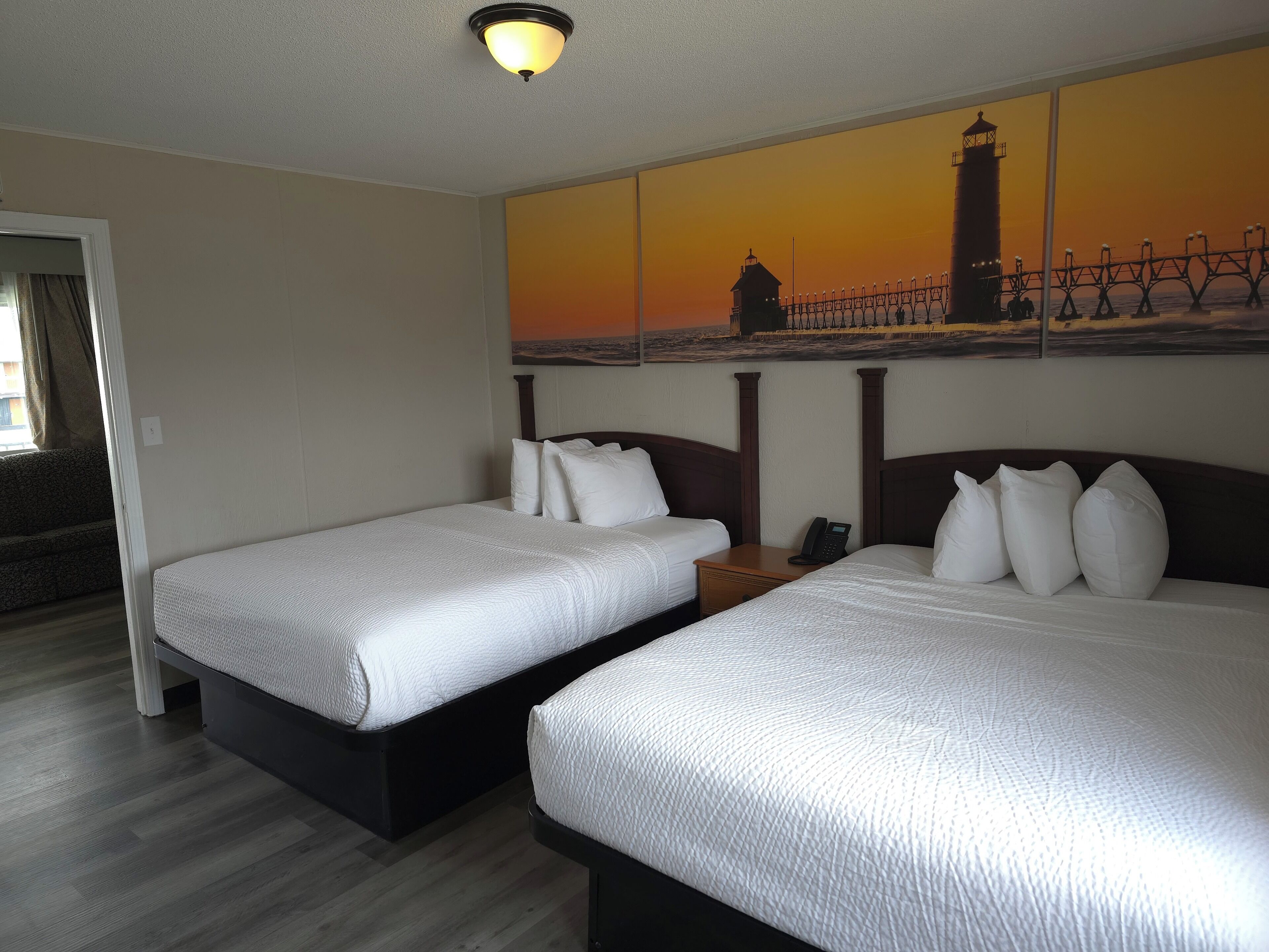 A hotel room with two beds, a painting of a lighthouse, and a phone on the nightstand.