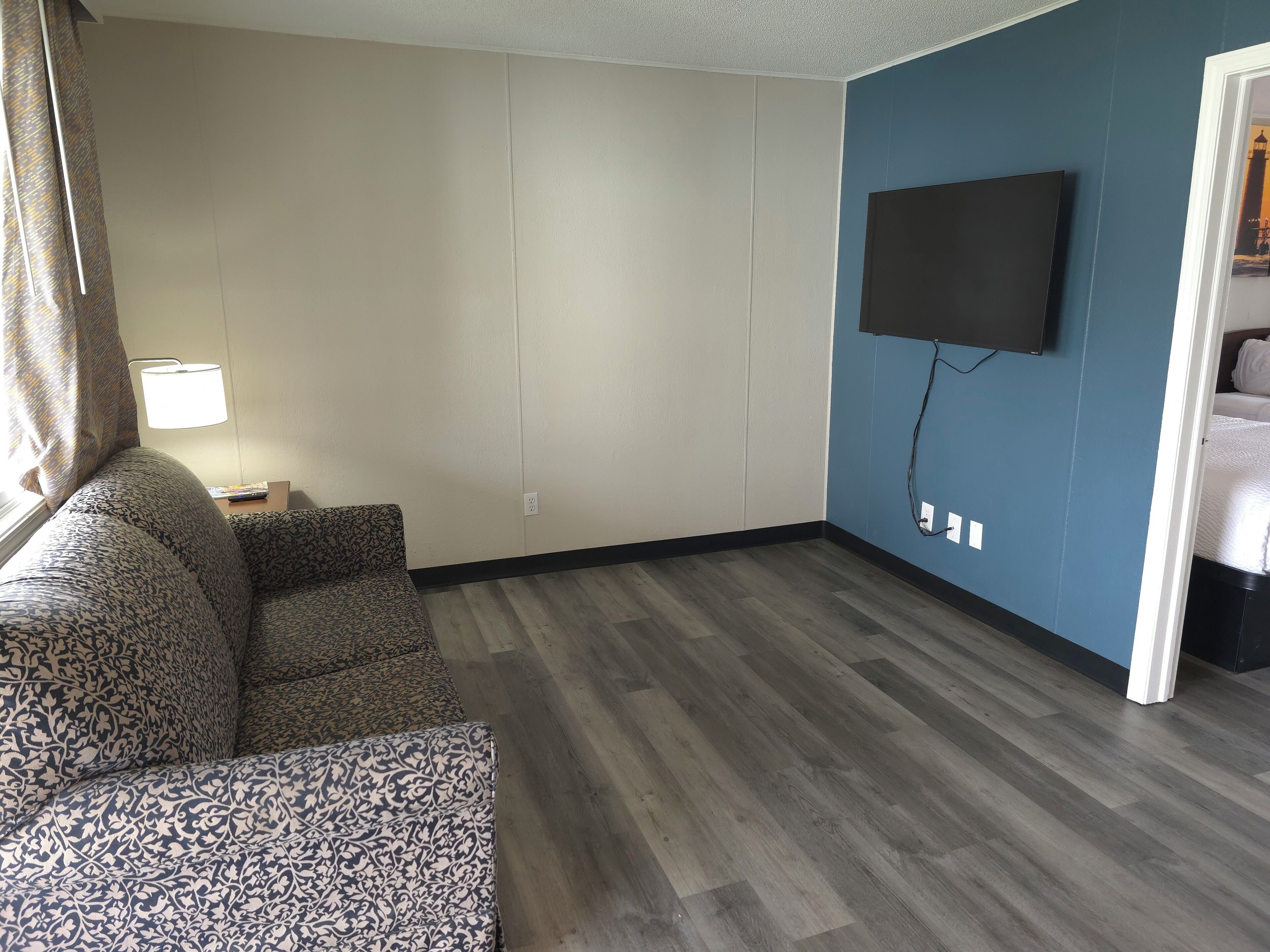Een woonkamer met een gestreept bankstel, een flatscreen televisie aan de wand en een raam met gordijnen.